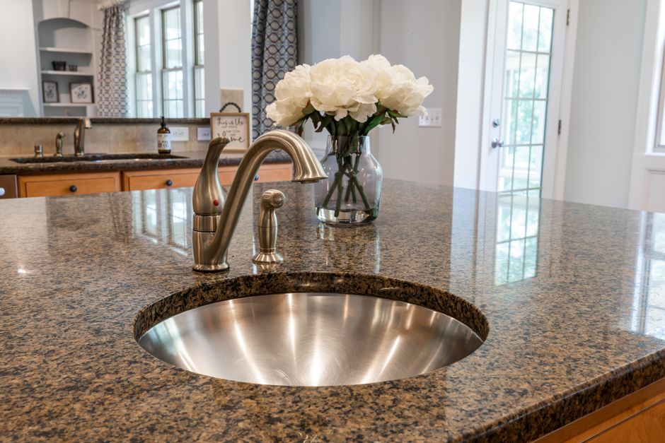 Kitchen with a granite countertop, a stainless steel sink and flowers in a vase.